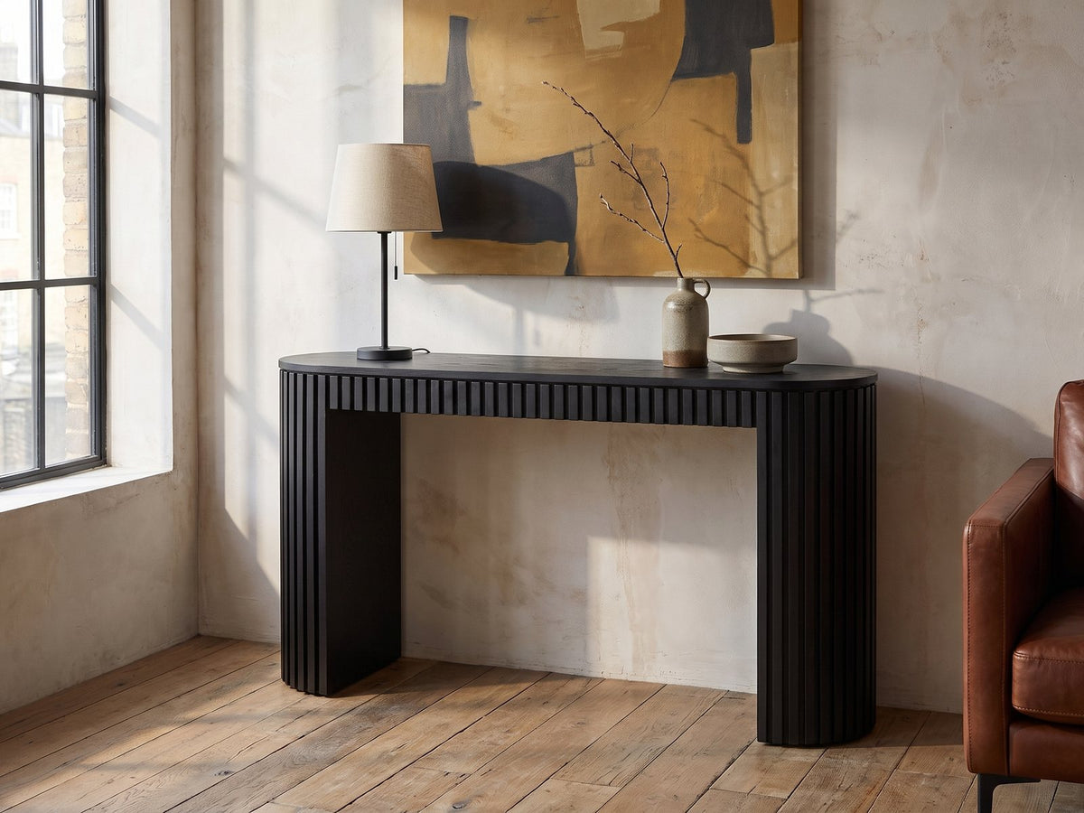 Monterosso Black Wood Veneer Fluted Oval Console Table against a plaster wall in an industrial loft