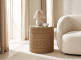 Montescaglioso Woven Seagrass Drum Side Table with a lamp and a ceramic bowl beside a cream boucle armchair in a bright plaster room