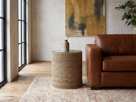 Montescaglioso Woven Seagrass Drum Side Table beside a leather sofa in an industrial loft