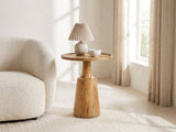 Montisi Natural Mango Pedestal Side Table with a lamp and a ceramic bowl beside a cream boucle armchair in a bright plaster room