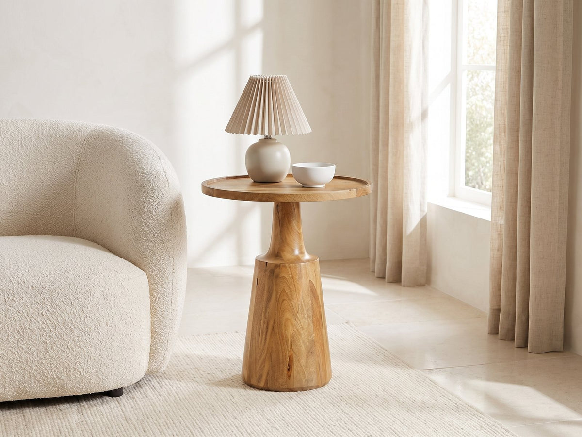 Montisi Natural Mango Pedestal Side Table with a lamp and a ceramic bowl beside a cream boucle armchair in a bright plaster room