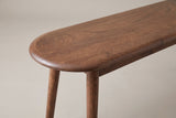 One end of the Montone bench: the half-round end of the oak top with its rounded edge, the slim apron and the round legs below