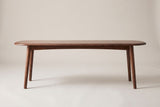 The Montone walnut-stained oak bench, side view on a light studio backdrop