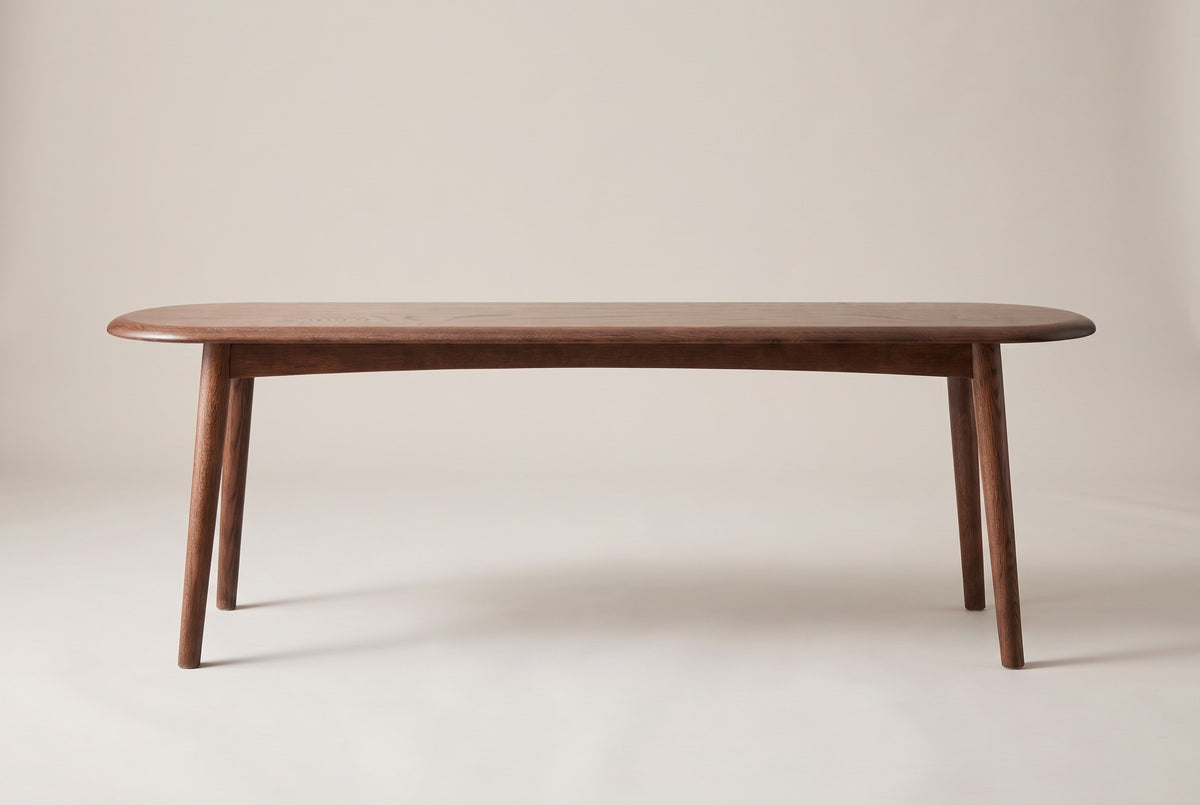 The Montone walnut-stained oak bench, side view on a light studio backdrop