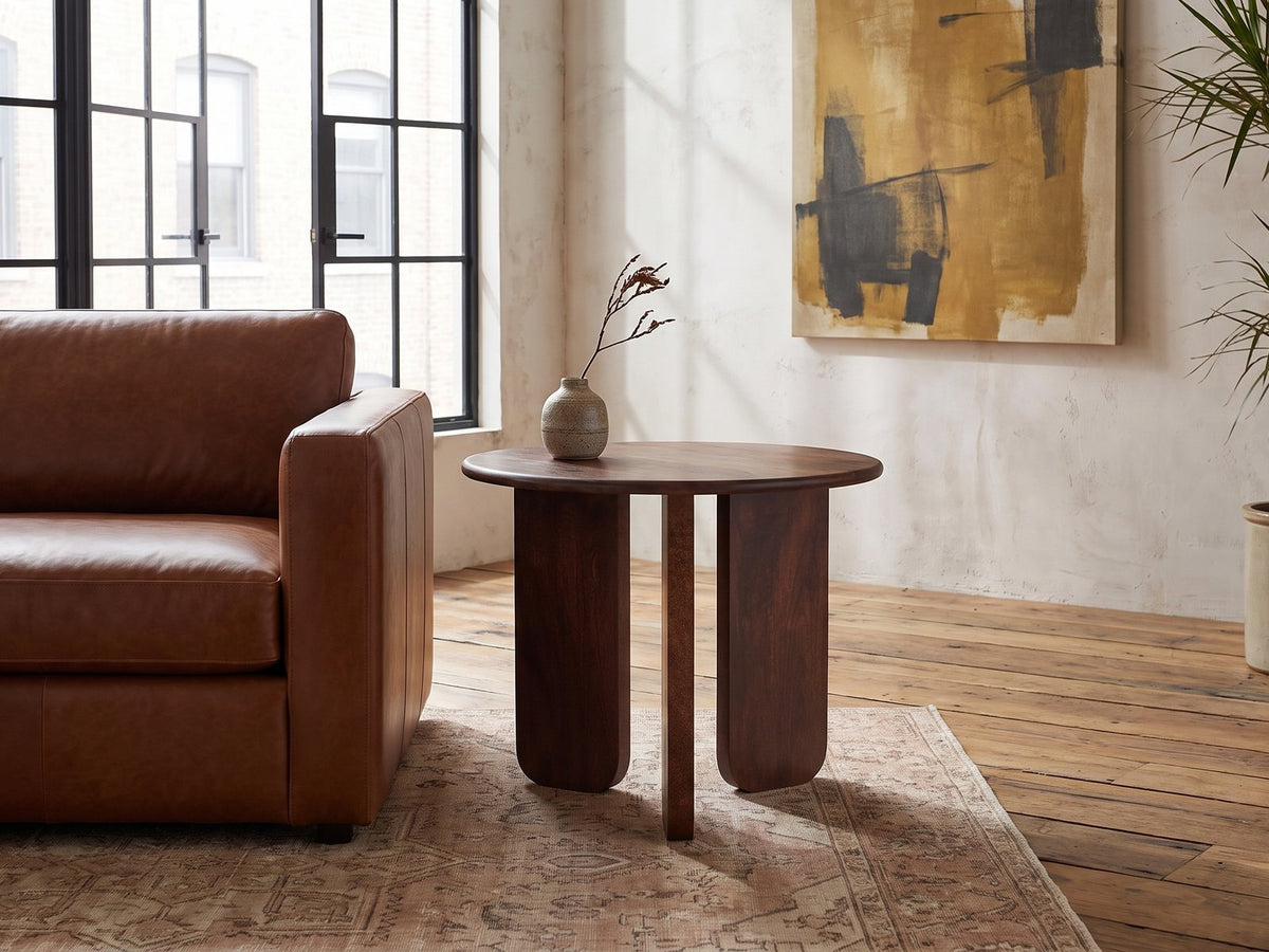 Morciano Mango Wood Round Side Table beside a leather sofa in an industrial loft