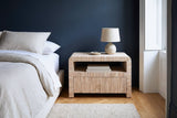 Muravera grasscloth nightstand with a ceramic lamp and two books against a deep indigo-navy wall in a Brooklyn brownstone bedroom with a herringbone oak floor