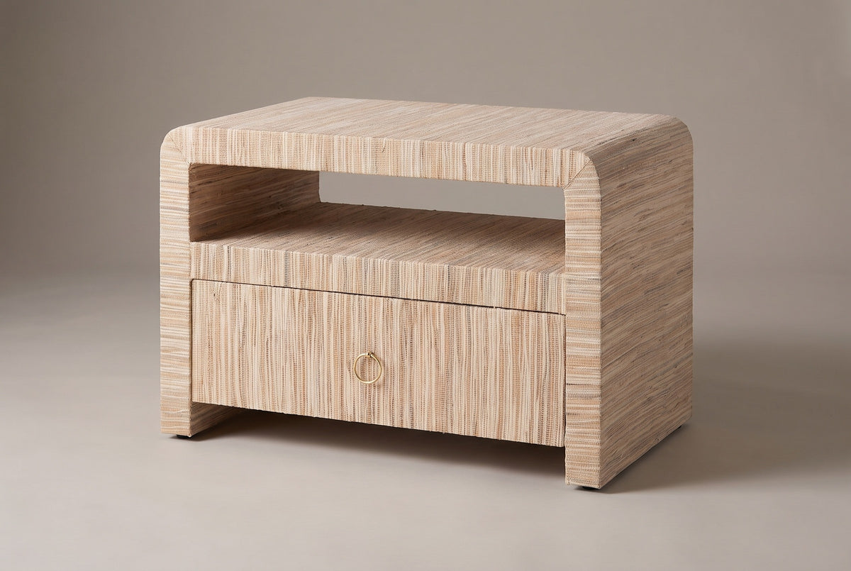 The Muravera one-drawer nightstand wrapped in natural woven grasscloth, with an open shelf, a ring pull and two thick side panels, three-quarter view on a light studio backdrop