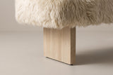 Where one Narni leg meets the seat: the long sheepskin locks hang over the top of a flat wood slab with a wire-brushed finish and a small black glide at its foot