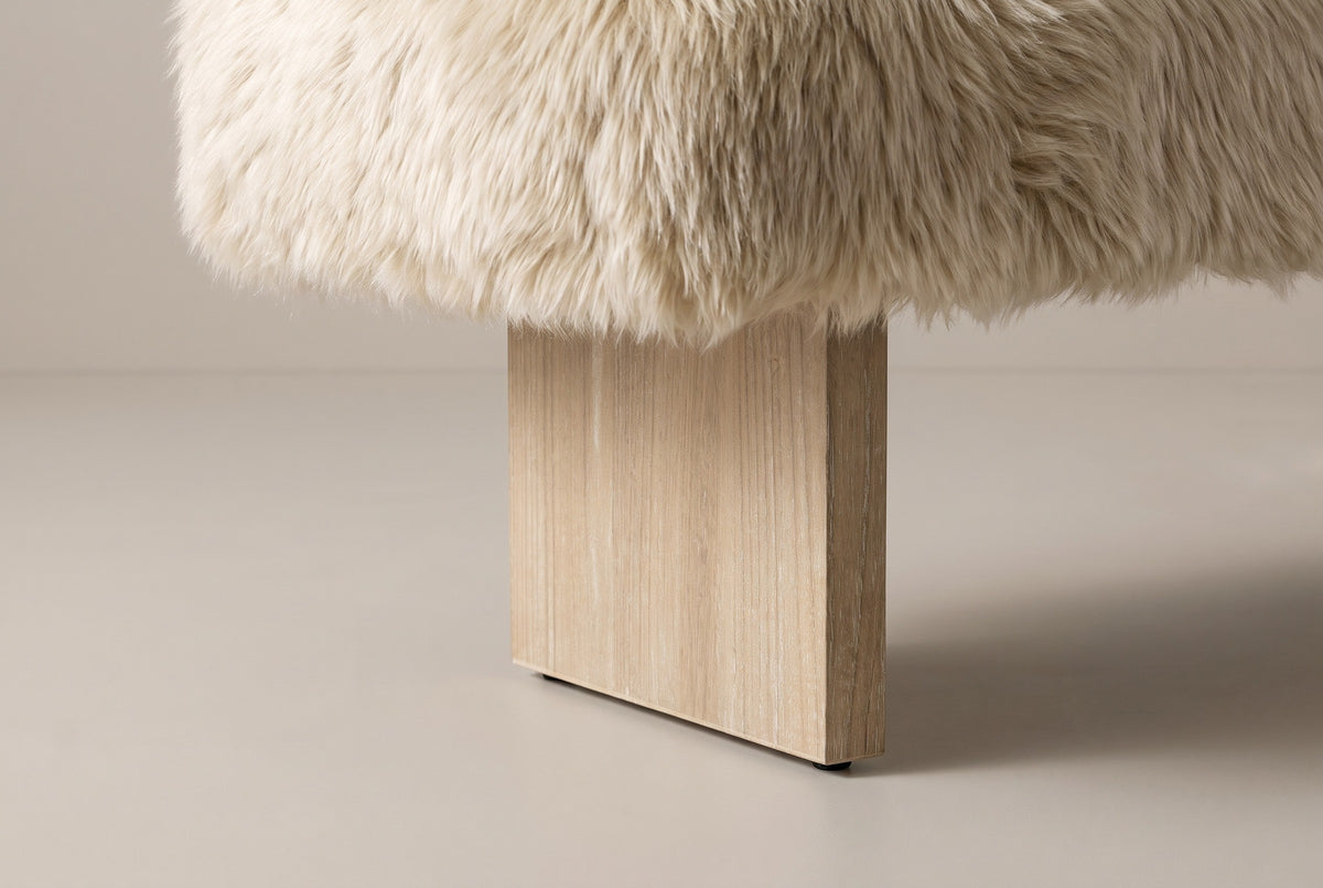 Where one Narni leg meets the seat: the long sheepskin locks hang over the top of a flat wood slab with a wire-brushed finish and a small black glide at its foot
