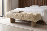 Narni sheepskin bench with a folded linen blanket at the foot of a white-linen bed in a Los Angeles bedroom with a walnut slat wall and a pale concrete floor