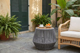 Naro rope side table with a coffee cup and a bowl of satsumas beside a rattan armchair in a New Orleans courtyard, an ochre plaster wall with green shutters and slate flagstones (chair and decor not included)