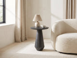 Navelli Graphite Cast Aluminum Pedestal Side Table with a lamp and a ceramic bowl beside a cream boucle armchair in a bright plaster room