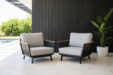 Two Naxos outdoor accent chairs on pale travertine in a covered lanai near Sarasota, a charcoal cypress board wall behind (plant not included)