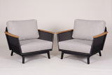 The pair of Naxos outdoor accent chairs in black aluminum with teak armrests and light grey cushions, three-quarter view on a light studio backdrop