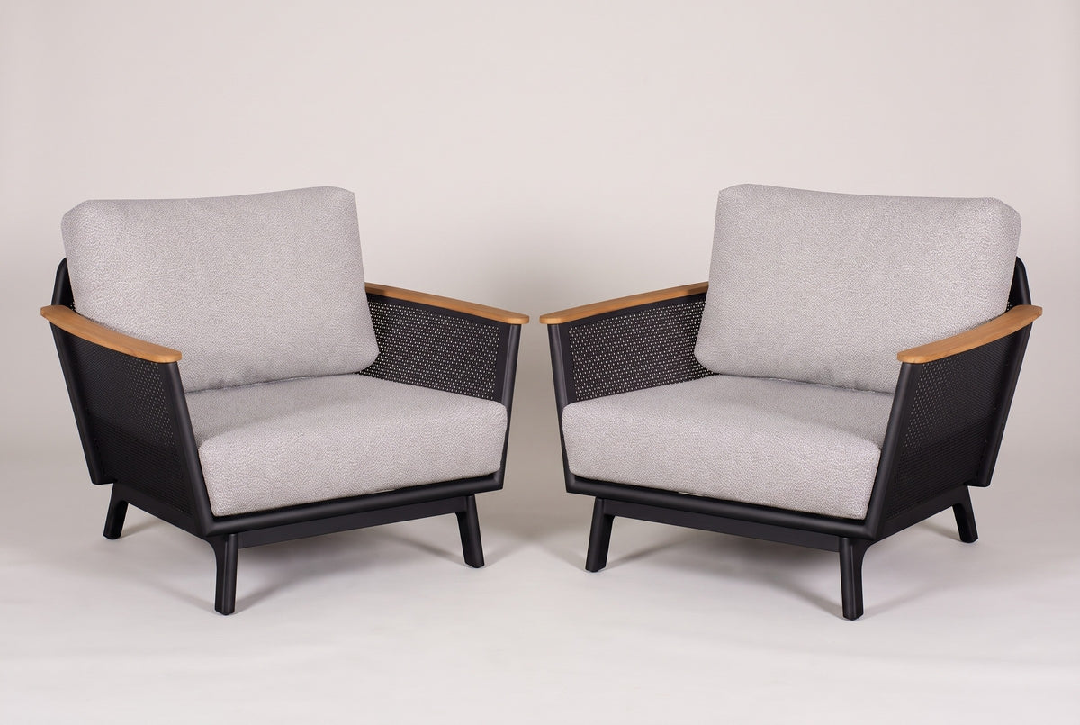 The pair of Naxos outdoor accent chairs in black aluminum with teak armrests and light grey cushions, three-quarter view on a light studio backdrop