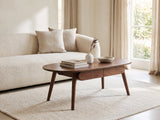 Neive 47-Inch Oval Walnut-Stained Solid Oak Coffee Table with 2 Drawers styled with books, a vase and a stone bowl in front of a cream sofa in a bright plaster room