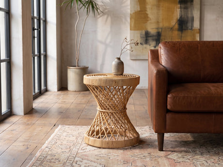 Neviano Natural Rattan Hourglass Side Table beside a cognac leather armchair in an industrial loft