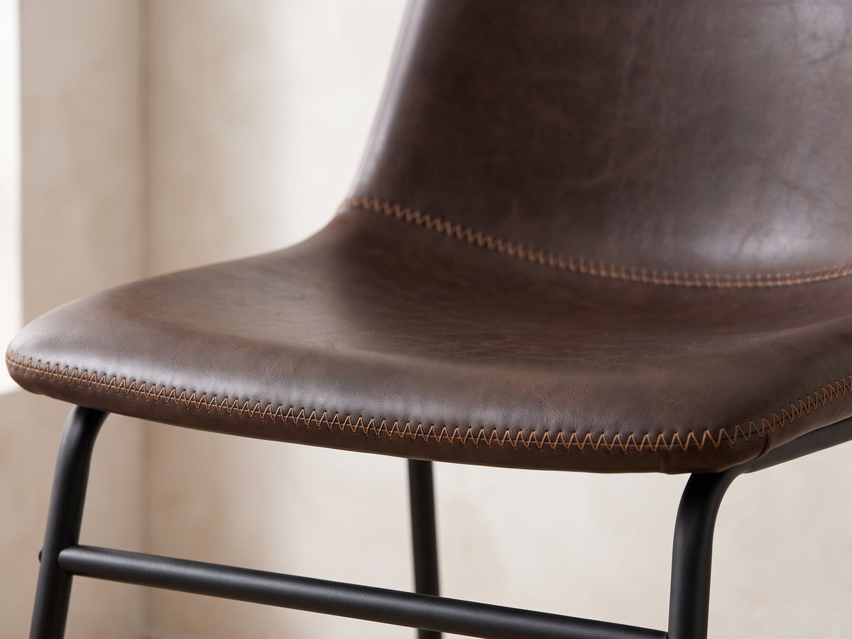 Close-up of the Nicastro 64-Inch Antique Black Farmhouse Dining Set with 4 Chairs: the dark-brown faux leather seat with its tan zigzag stitching
