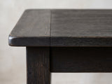 Close-up of the Nicastro 64-Inch Antique Black Farmhouse Dining Set with 4 Chairs: the rounded breadboard corner of the antique-black top above a square leg