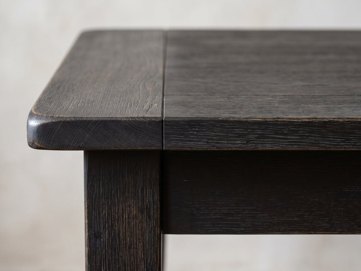 Close-up of the Nicastro 64-Inch Antique Black Farmhouse Dining Set with 4 Chairs: the rounded breadboard corner of the antique-black top above a square leg