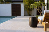 Nicolosi matte black studded concrete side table on a travertine pool deck in Naples, Florida, a white wall, bamboo and a teak lounger behind (lounger not included)