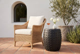 Nicolosi matte black studded side table on terracotta tiles at a Santa Barbara terrace with a white plaster wall and an olive tree, beside a woven armchair (chair, glass and vase not included)