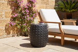 Nicolosi matte black studded side table in a St. Augustine courtyard with a coquina stone wall and bougainvillea, beside a teak lounger (lounger, glass and cherries not included)