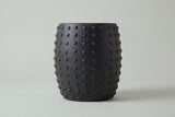 The Nicolosi side table seen straight from the side: a gently rounded barrel with studs along both edges
