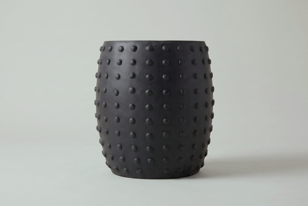 The Nicolosi side table seen straight from the side: a gently rounded barrel with studs along both edges