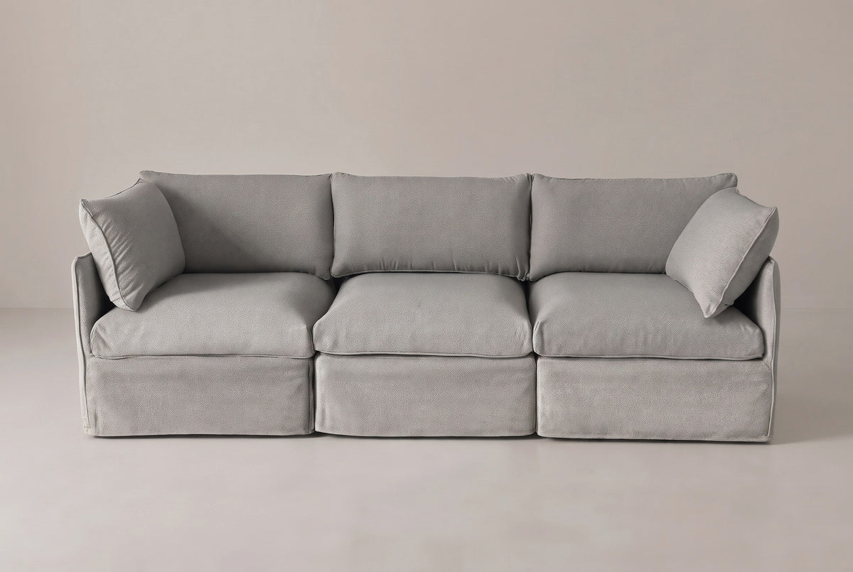 The Nicosia modular sofa from the front: three grey slipcovered seats, two low arms and two corner throw pillows