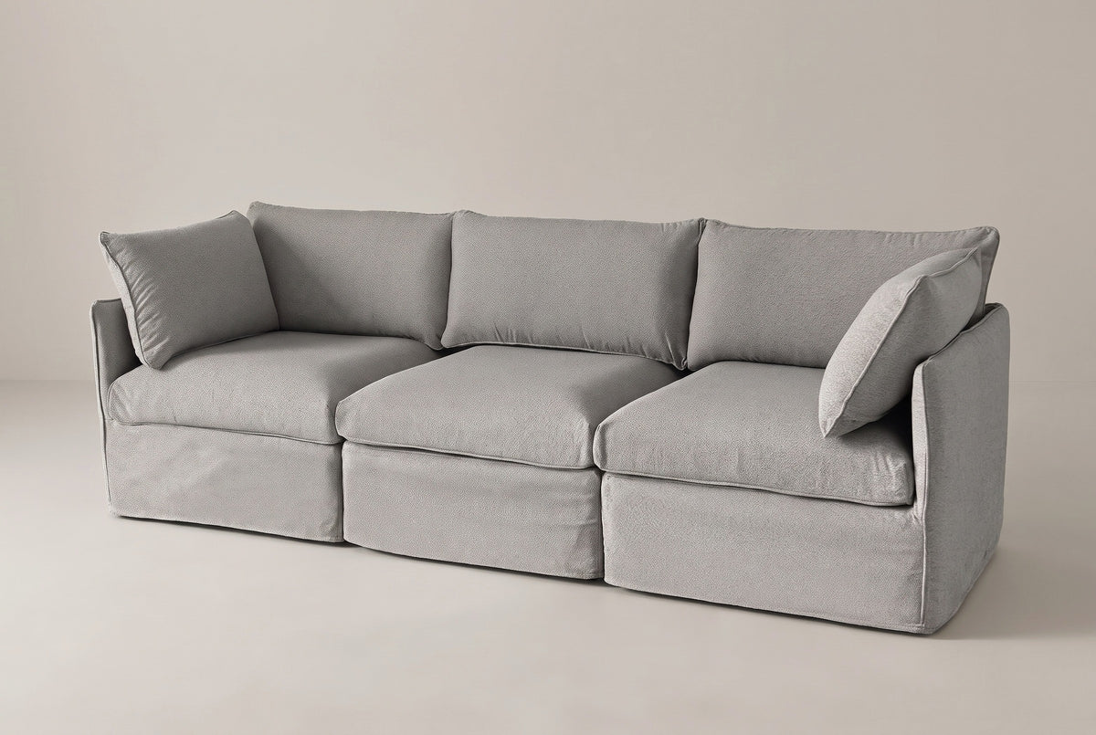 The Nicosia slipcovered modular sofa in grey, three-quarter view on a light studio backdrop