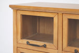 The top-left door of the Noci cabinet under the overhanging top with its cove moulding: mitred pine frame, clear glass, and the bronze-finish pull on the bottom rail