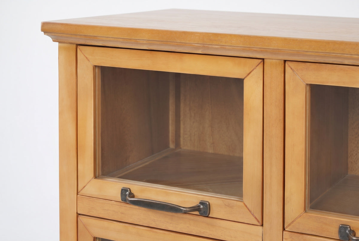 The top-left door of the Noci cabinet under the overhanging top with its cove moulding: mitred pine frame, clear glass, and the bronze-finish pull on the bottom rail