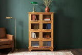 Noci pine display cabinet with a brass desk lamp and books behind its glass doors against a deep forest-green plaster wall in a Portland study with a walnut floor