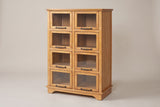 The Noci pine display cabinet in honey pine with eight glass doors and bronze-finish pulls, three-quarter view on a light studio backdrop