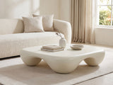 Noli White Sculpted Fiberglass Coffee Table styled with books, a vase and a stone bowl in front of a cream sofa in a bright plaster room
