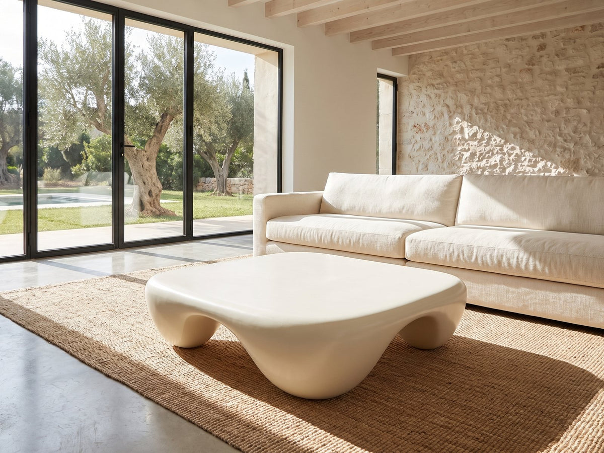 Noli White Sculpted Fiberglass Coffee Table on a jute rug in front of a linen sofa in a poolside villa