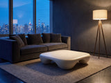 Noli White Sculpted Fiberglass Coffee Table on a wool rug in front of a velvet sofa in a city penthouse at blue hour