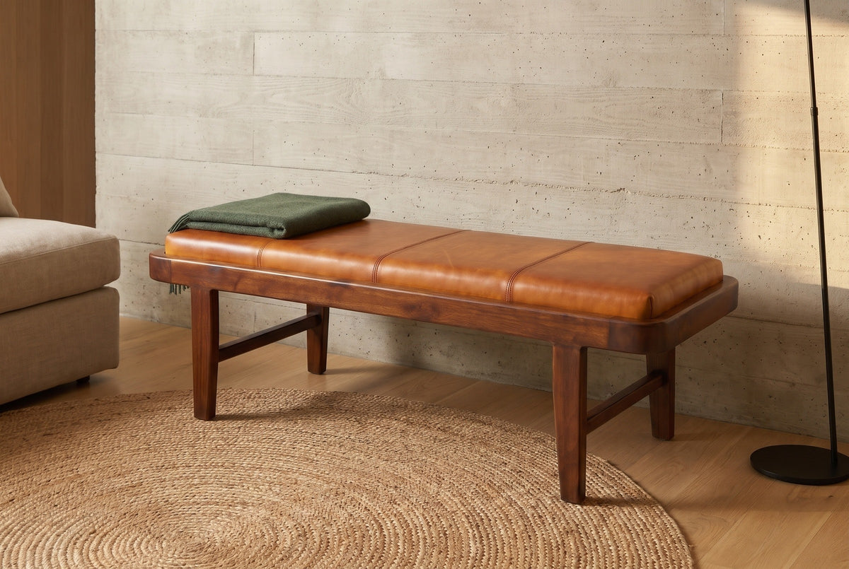 Norcia tan leather bench against a pale board-formed concrete wall in a Los Angeles living room with a round jute rug and a green wool throw