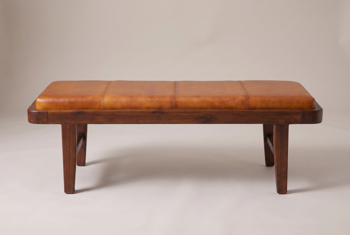 The Norcia bench, front view on a light studio backdrop: four panels across the tan leather cushion, a wood tray and four legs