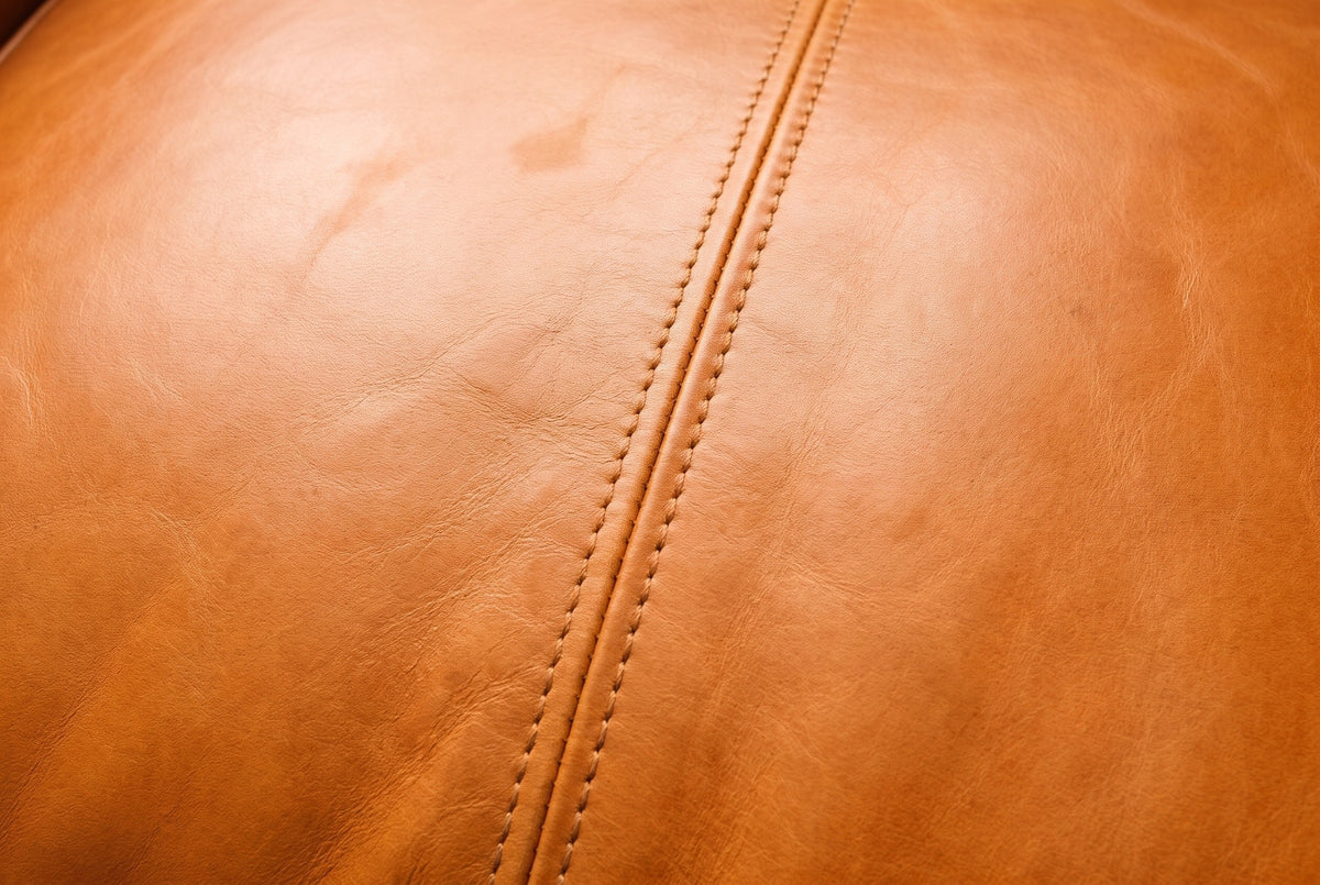 Close-up of the genuine leather on the Norcia bench: warm saddle tan leather with fine natural grain and a welted seam with saddle stitching on each side