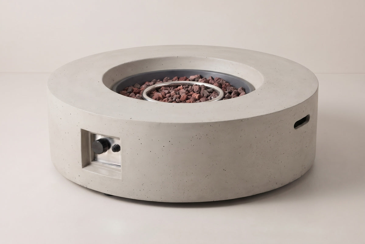 The Noto round fire pit in light gray concrete, three-quarter view on a light studio backdrop, with the control niche on the front and a handle slot in the side