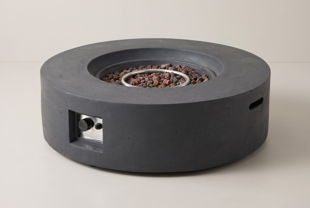 The Noto round fire pit in dark gray concrete, three-quarter view on a light studio backdrop, with the control niche on the front and a handle slot in the side
