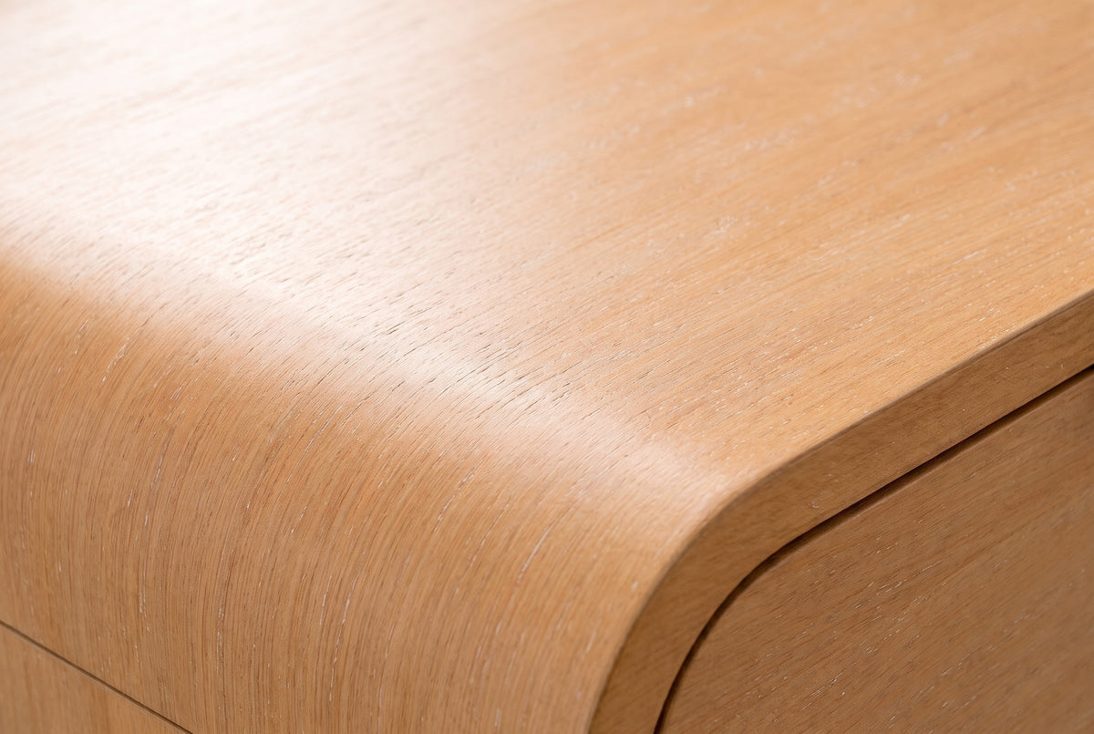 Close-up of the Nuoro nightstand top: caramel maple wood veneer with fine straight grain and faint pale flecks, flowing over the rounded waterfall edge