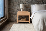 Nuoro Caramel Waterfall nightstand with a ceramic lamp and a seagrass basket against a dry-stacked fieldstone wall in a Telluride bedroom with a smoked oak floor and a wool rug