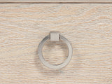 Close-up of the Oderzo 36-Inch Washed Oak 5-Drawer Chest: a polished nickel ring pull on a washed oak drawer, under the stepped mitred moulding