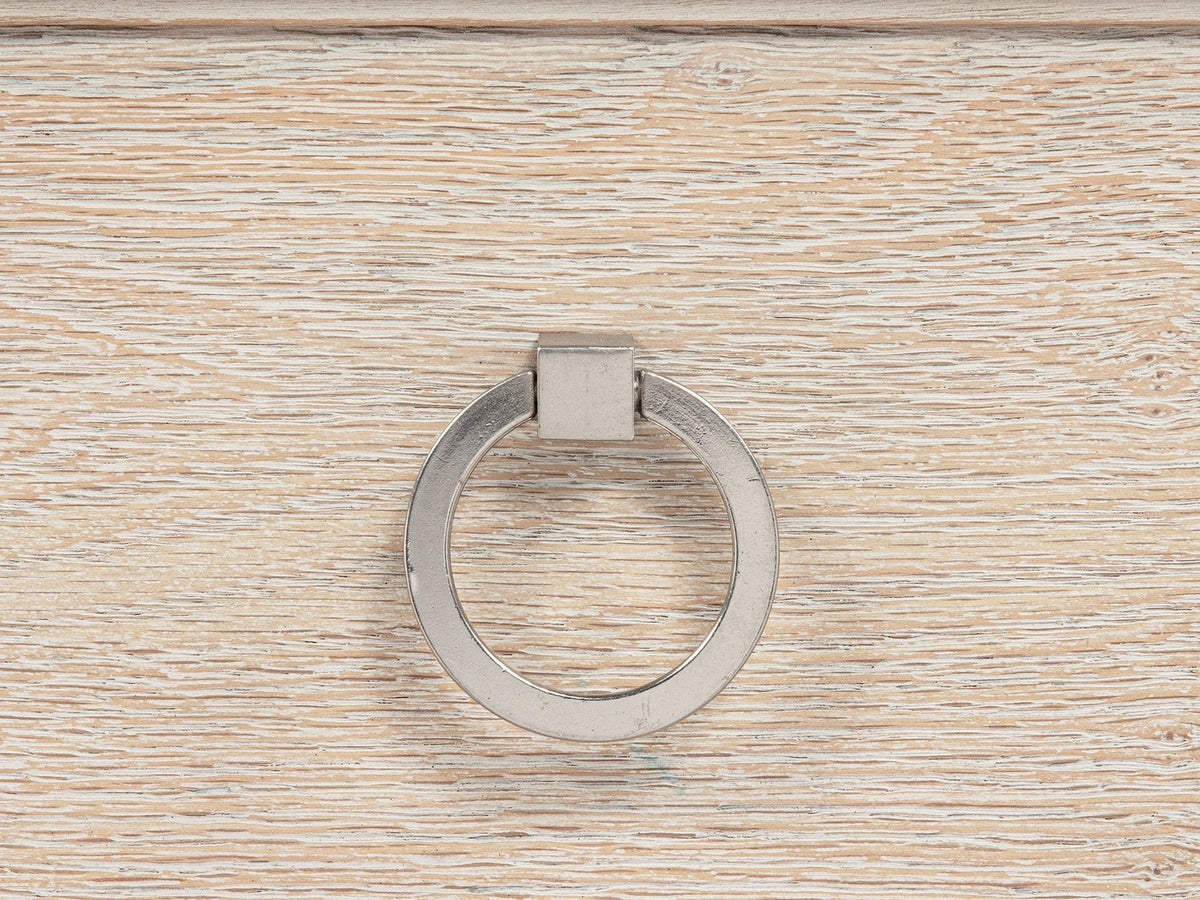 Close-up of the Oderzo 36-Inch Washed Oak 5-Drawer Chest: a polished nickel ring pull on a washed oak drawer, under the stepped mitred moulding