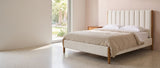 Ofena white boucle channel bed against a blush-pink plaster wall in a Palm Springs bedroom, a tall glass door at the left looking onto a sunlit garden with a palm, Queen shown
