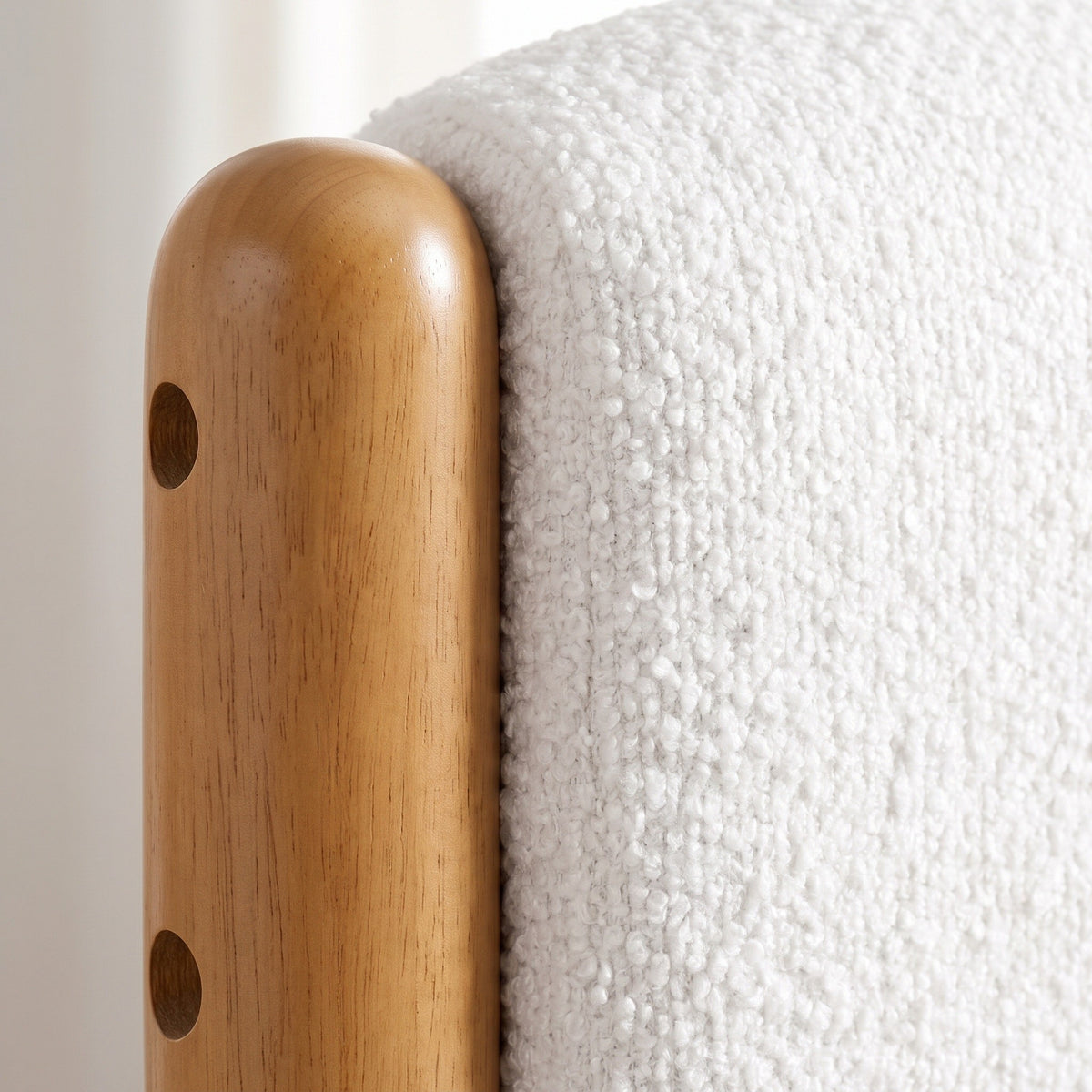 Close-up of the Ofena bed where a honey-finish rubberwood post with two small bolt covers meets the white boucle of the headboard