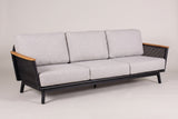 The Ognina outdoor sofa in black aluminum with teak armrests and light grey cushions, three-quarter view on a light studio backdrop